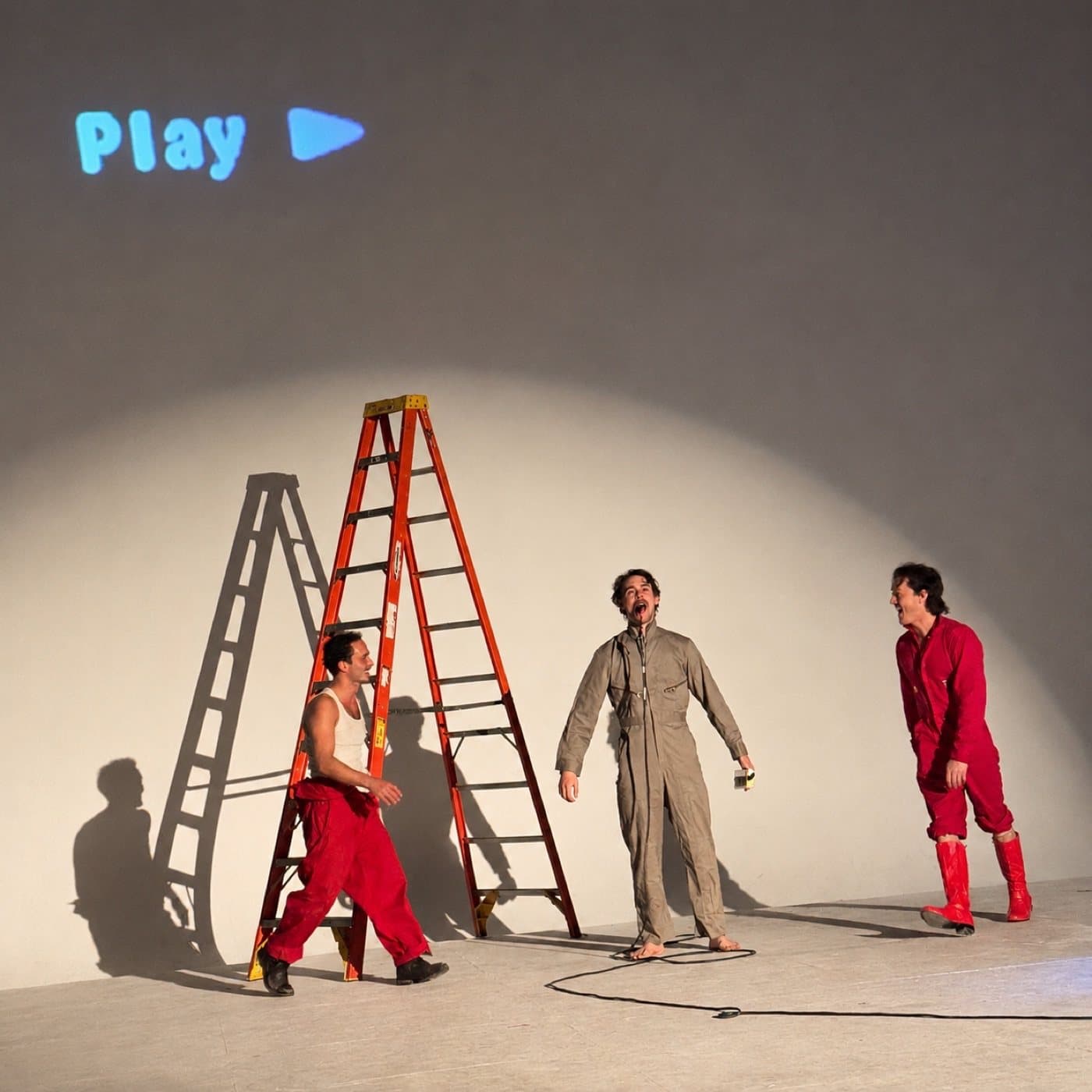 Three performers on stage under a projected play symbol